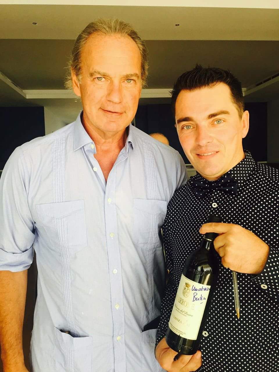 Mario Andries, con pajarita de lunares, junto a Bertin Osborne en un restaurante. Entre los dos sostienen una botella de Ribera del Duero firmada con una dedicatoria en la etiqueta; Mario lleva todavia el boligrafo en la mano.